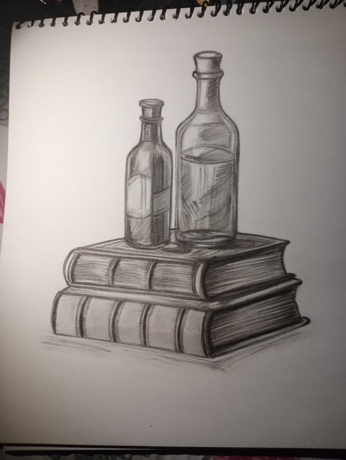 Pencil still life of two glass bottles on a stack of leather books